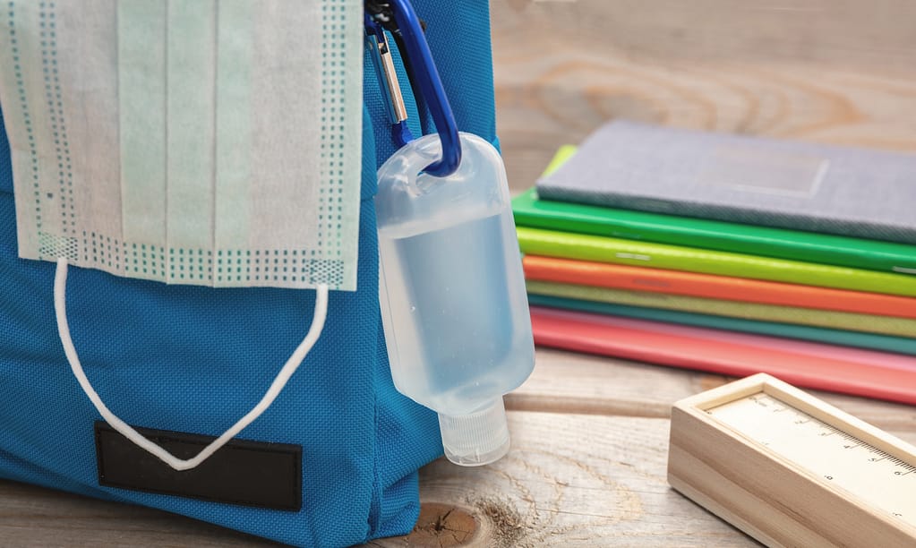 Sanitizer gel and medical mask on a blue color school bag