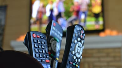 TV remotes with a television with people playing football. Watching movies, sports or TV shows