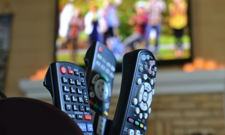 TV remotes with a television with people playing football. Watching movies, sports or TV shows